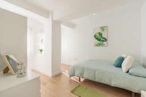 A bedroom with a bed, a green rug, a wall-mounted plant, and a framed picture on a bedside table.