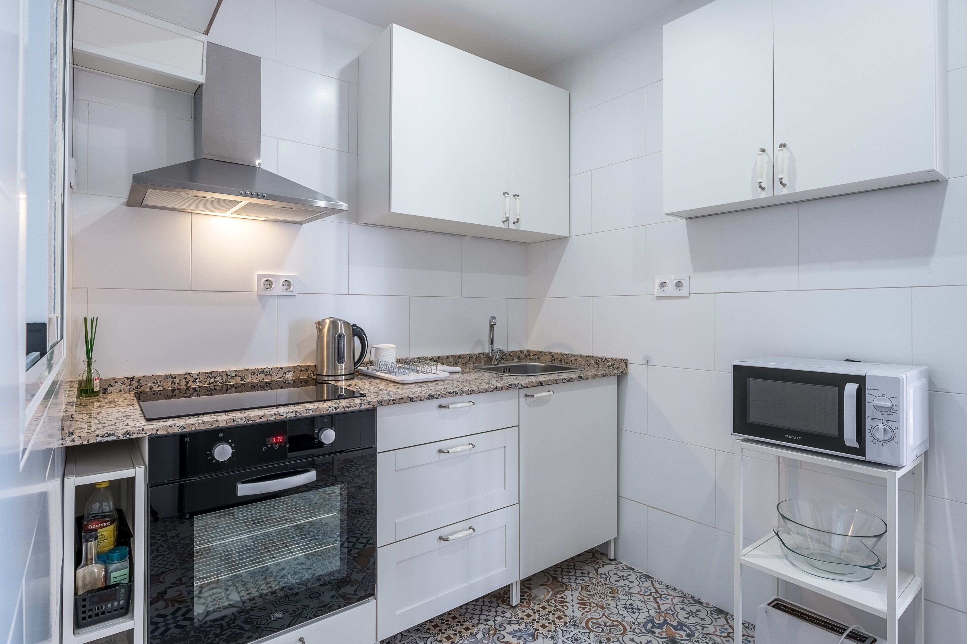 A kitchen with white cabinets, a stainless steel range hood, a microwave, and a glass bowl on a white shelf.