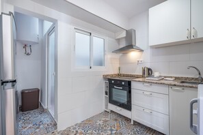 A modern kitchen with white cabinets, a built-in oven, a stainless steel range hood, and a patterned tile floor.