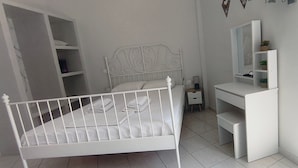 Quarto branco com uma cama, mesa de cabeceira, espelho e armário embutido.