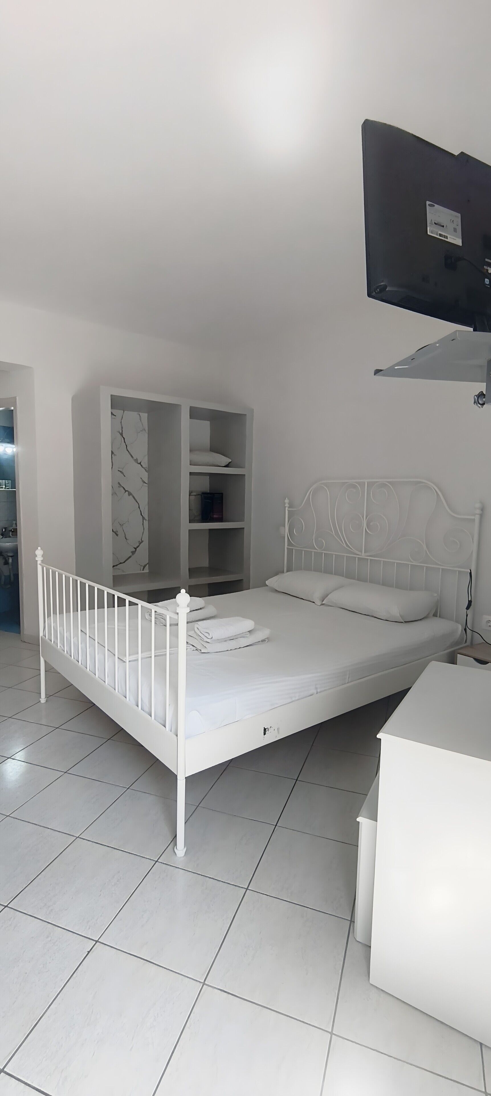 Un lit en métal blanc avec une tête de lit, une table de chevet blanche et une armoire blanche, le tout placé devant un mur à motifs de marbre.