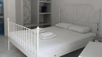 Un lit en métal blanc avec une tête de lit, une table de chevet blanche et une armoire blanche, le tout placé devant un mur à motifs de marbre.