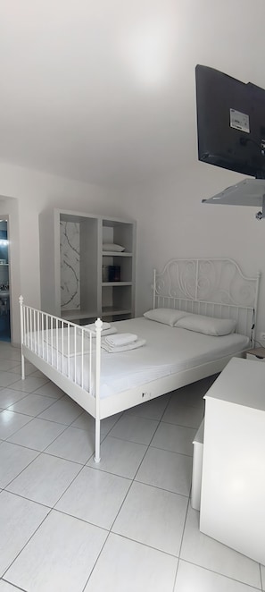 A white metal bed with a headboard, a white bedside table, and a white wardrobe with a marble-patterned wall behind it. - Studio Apartment 'Merichas 7 Irida' with Mountain View, Wi-Fi and Air Conditioning (Mérichas)