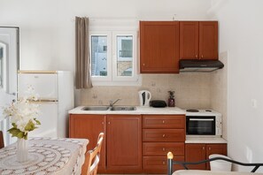 A kitchen with wooden cabinets, a microwave, a kettle, and a sink.
