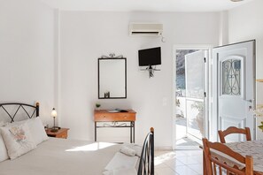Une chambre à coucher comprenant un lit, une table de chevet, une lampe, une commode, un téléviseur et une porte donnant sur un espace extérieur.