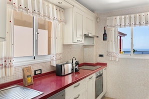 A kitchen with white cabinets, a red countertop, a toaster, and a bottle of wine on the wall.
