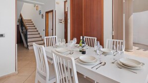 A dining area with a table set for four, white chairs, and a bottle of wine. - Holiday Apartment 'Obsidian Villa Bentayga' with Sea View and Wi-Fi (Adeje)
