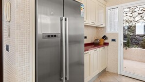 A stainless steel refrigerator in a kitchen with beige cabinets and a stone wall view. - Holiday Apartment 'Obsidian Villa Bentayga' with Sea View and Wi-Fi (Adeje)