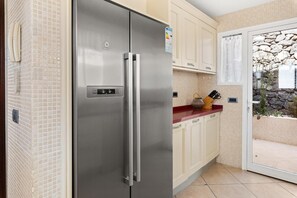 Un refrigerador de acero inoxidable en una cocina con gabinetes color crema y vista a una pared de piedra.