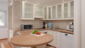 A modern kitchen with white cabinets, a microwave, a kettle, and a dishwasher.