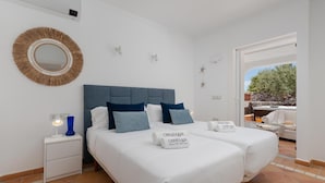 A double bed with white bedding and two pillows, a bedside table with a lamp, a round mirror, and a sign indicating a 'vacation rental' service.