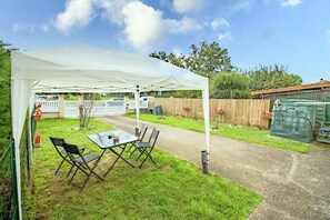 A covered patio area with a table and chairs, a white fence, and a wooden fence in the background. - Bright Apartment with Garden in the Heart of Le Bugue (Le Bugue)