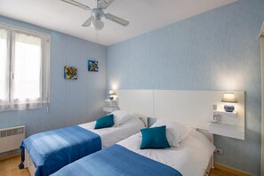 A hotel room with two beds, a ceiling fan, wall-mounted lamps, and a window with curtains. - Bright Apartment with Garden in the Heart of Le Bugue (Le Bugue)