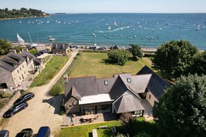 Una propiedad costera con una amplia terraza, edificios de piedra y vistas al mar con barcos.
