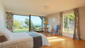 Ein Schlafzimmer mit Bett, Sessel, Tisch und Blick ins Freie.