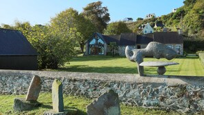 Eine Steinskulptur in einer grünen Umgebung mit einer Steinmauer und einem Haus im Hintergrund.