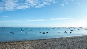 Ein Kiesstrand mit Booten auf ruhigem Wasser unter blauem Himmel.