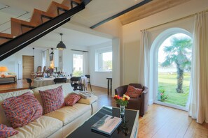 En rummelig opholdsstue med trappe, spiseplads og et stort vindue med udsigt til naturen.
