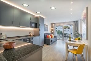 Une cuisine moderne avec des comptoirs en granit, un coin repas agrémenté d’une chaise jaune, et un espace de vie comprenant un canapé et une table.