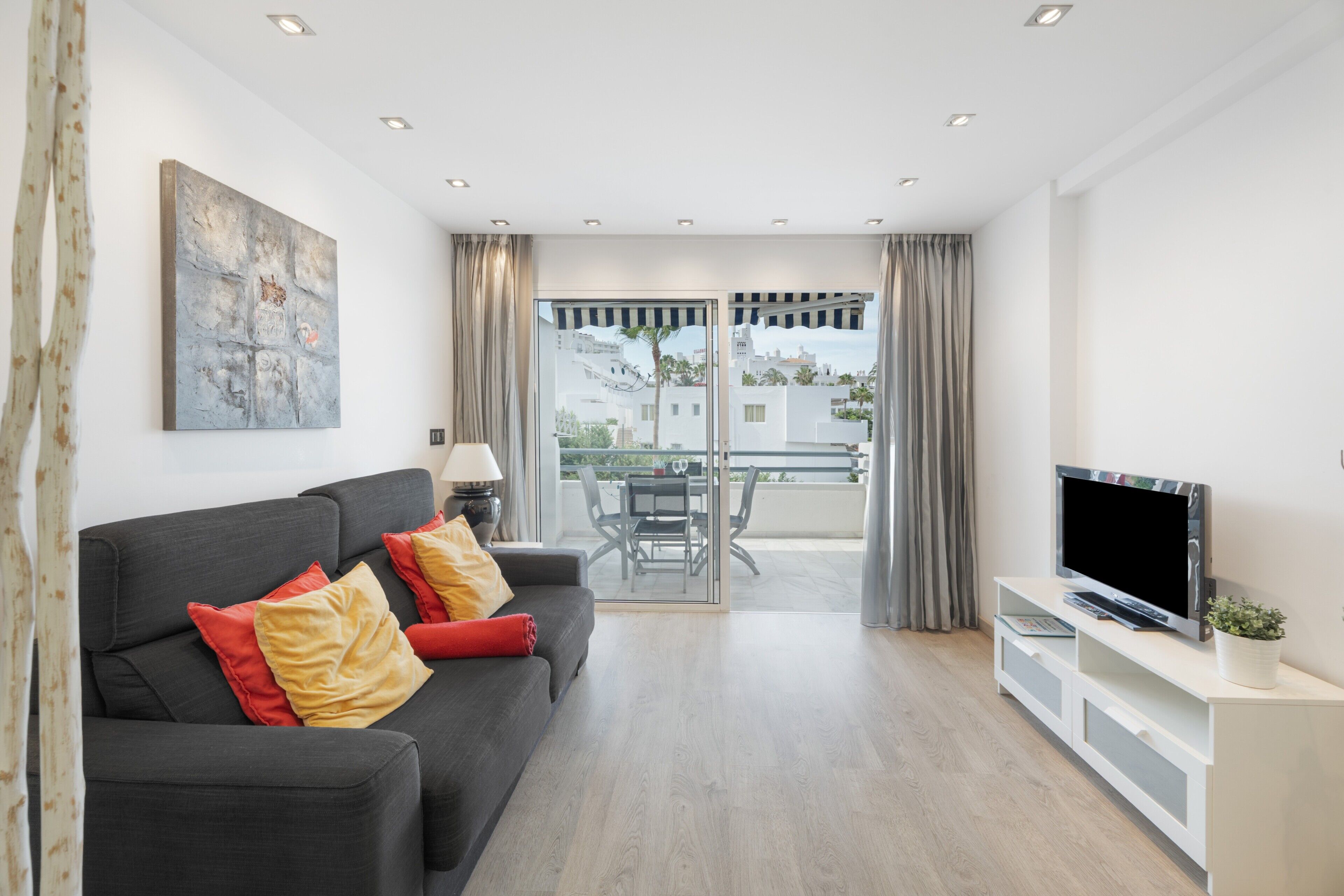 A modern living room with a sofa, TV, and balcony.