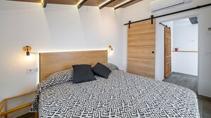 Une chambre à coucher moderne avec une couvre-lit à motifs, une tête de lit en bois et un plafond doté d’un éclairage encastré.