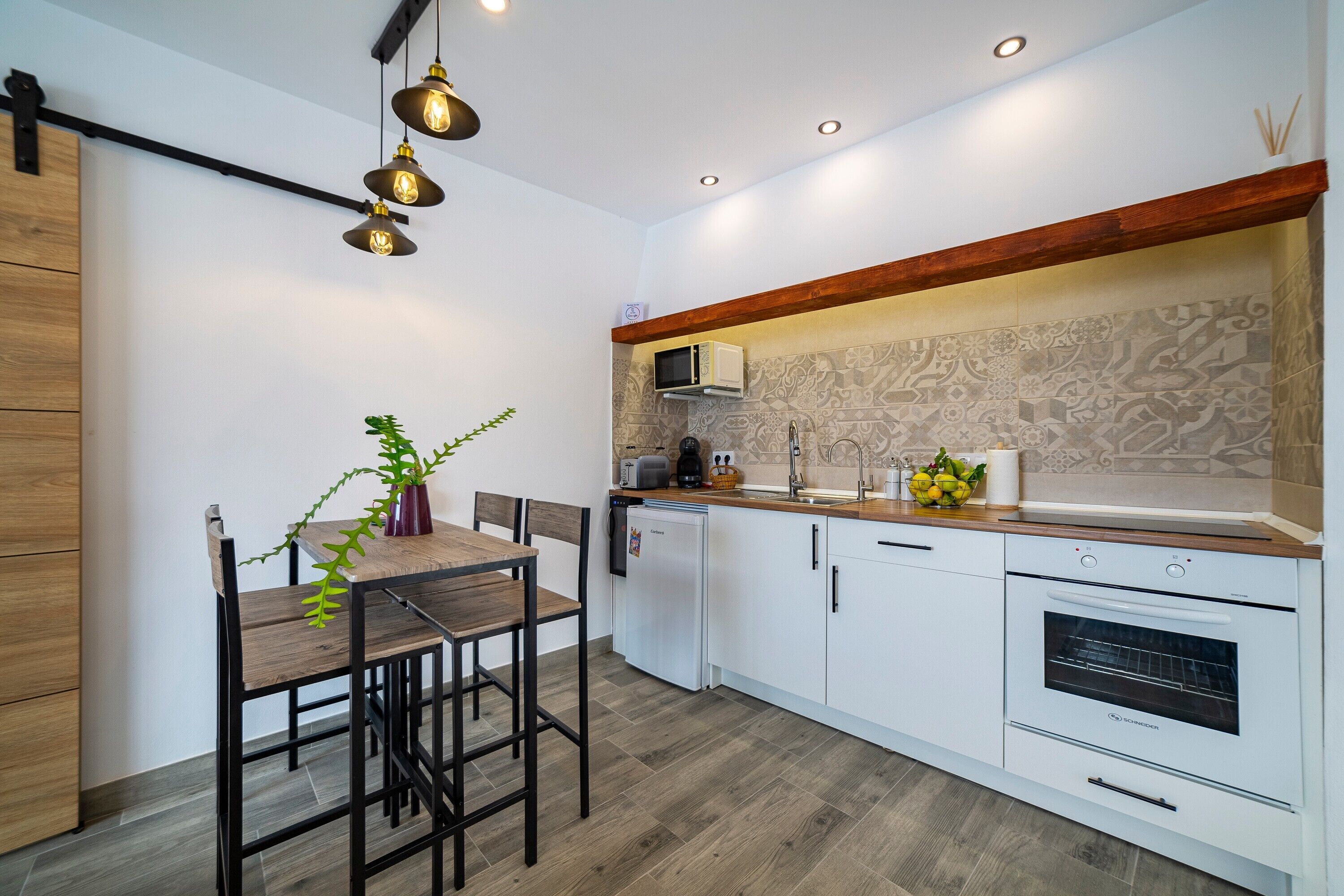 Eine moderne Küche mit Holztisch, weißen Schränken, einem eingebauten Backofen und Pendelleuchten.