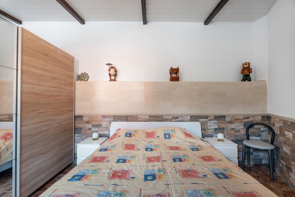 A bedroom with a bed, two bedside tables, a chair, a wooden wardrobe, and a wall-mounted shelf with decorative items. - Holiday Home 'Casa Boulou' in El Roque with Private Pool and Fiber Optic Wi-Fi (El Rincón)