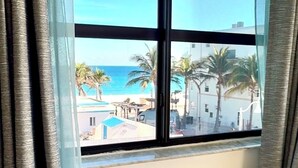 A room with a large window overlooking a beach and palm trees. - Newly renovated apartment with ocean views, steps from the beach and Boardwalk! (Hollywood)