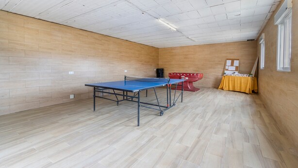 Una habitación con mesa de ping pong, una mesa de tenis de mesa roja y una mesa amarilla con un cartel.