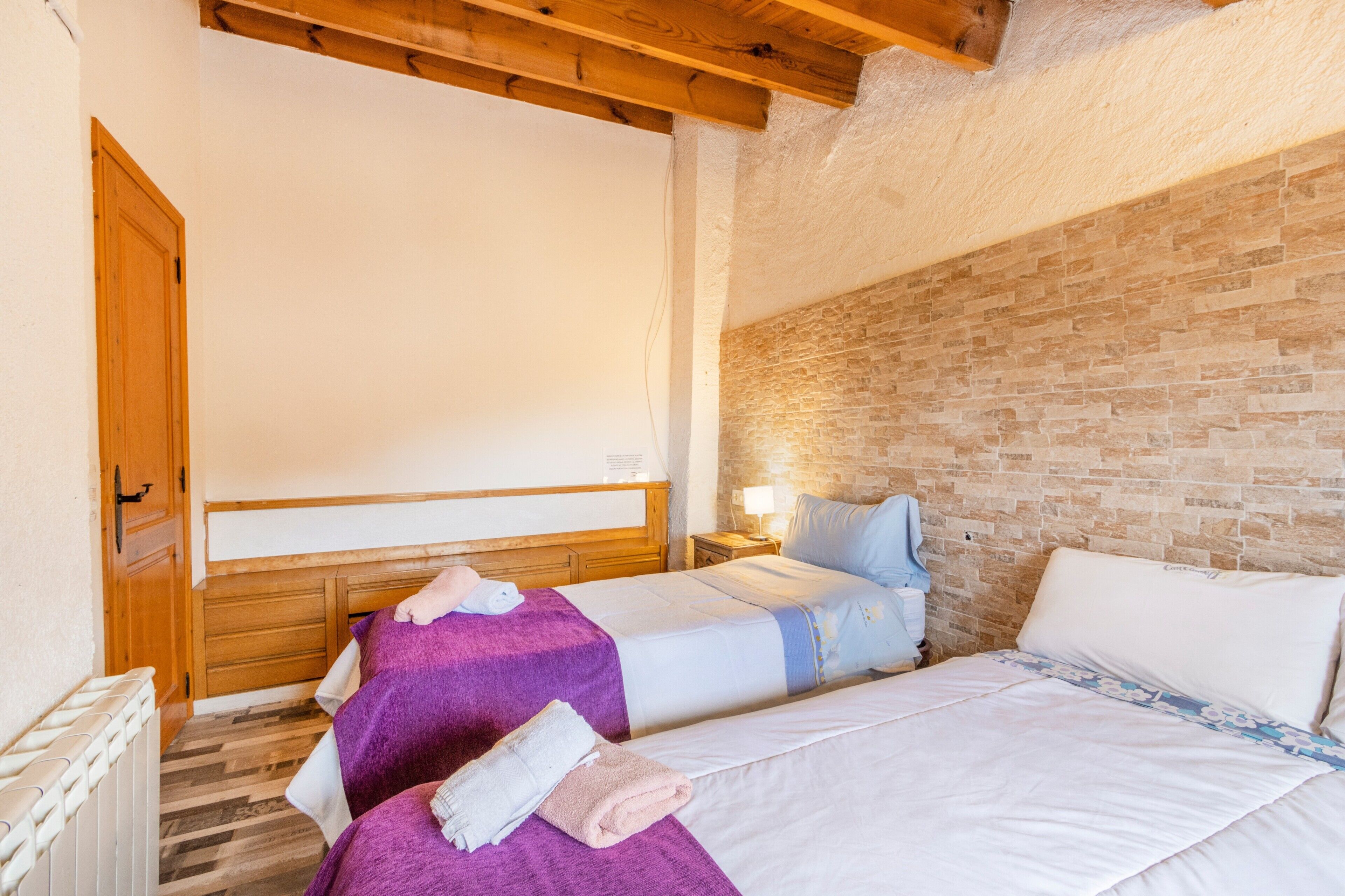 Un dormitorio con dos camas, una pared de ladrillo, vigas de madera y una puerta de madera.