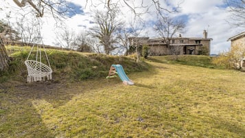 A grassy outdoor area with a swing, a slide, and a building in the background.