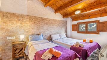 A room with two beds, wooden ceiling beams, a brick wall, and a window with a view.