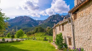 Un edificio de piedra con jardín y montañas al fondo.