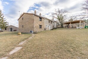 Una casa de piedra con un espacio exterior cubierto, un sendero pavimentado y un patio con césped.
