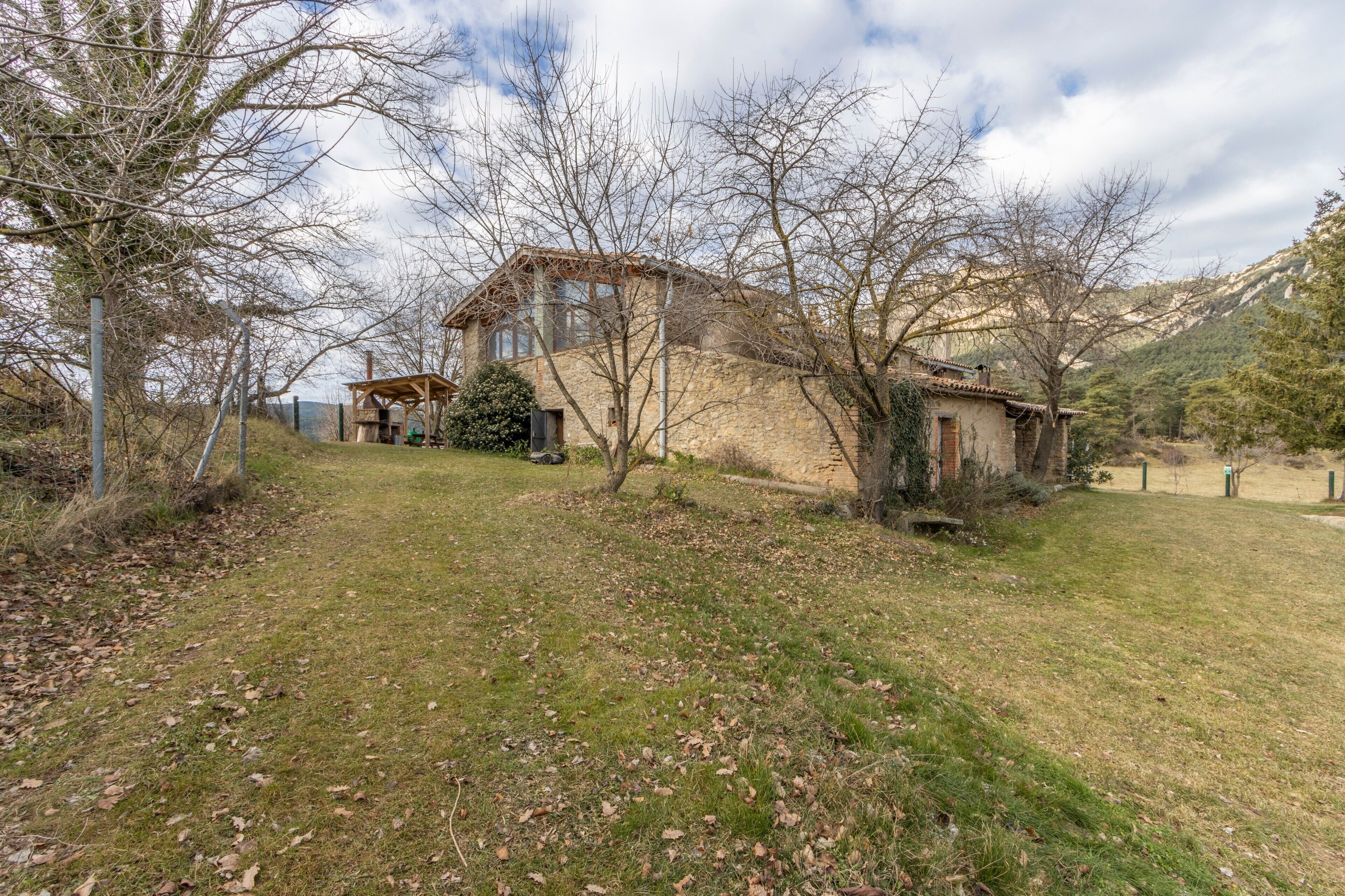 A stone house with a wooden structure, surrounded by trees and a grassy area.