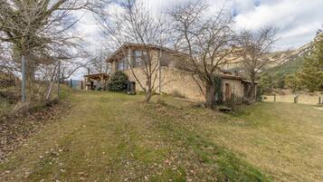 A stone house with a wooden structure, surrounded by trees and a grassy area.