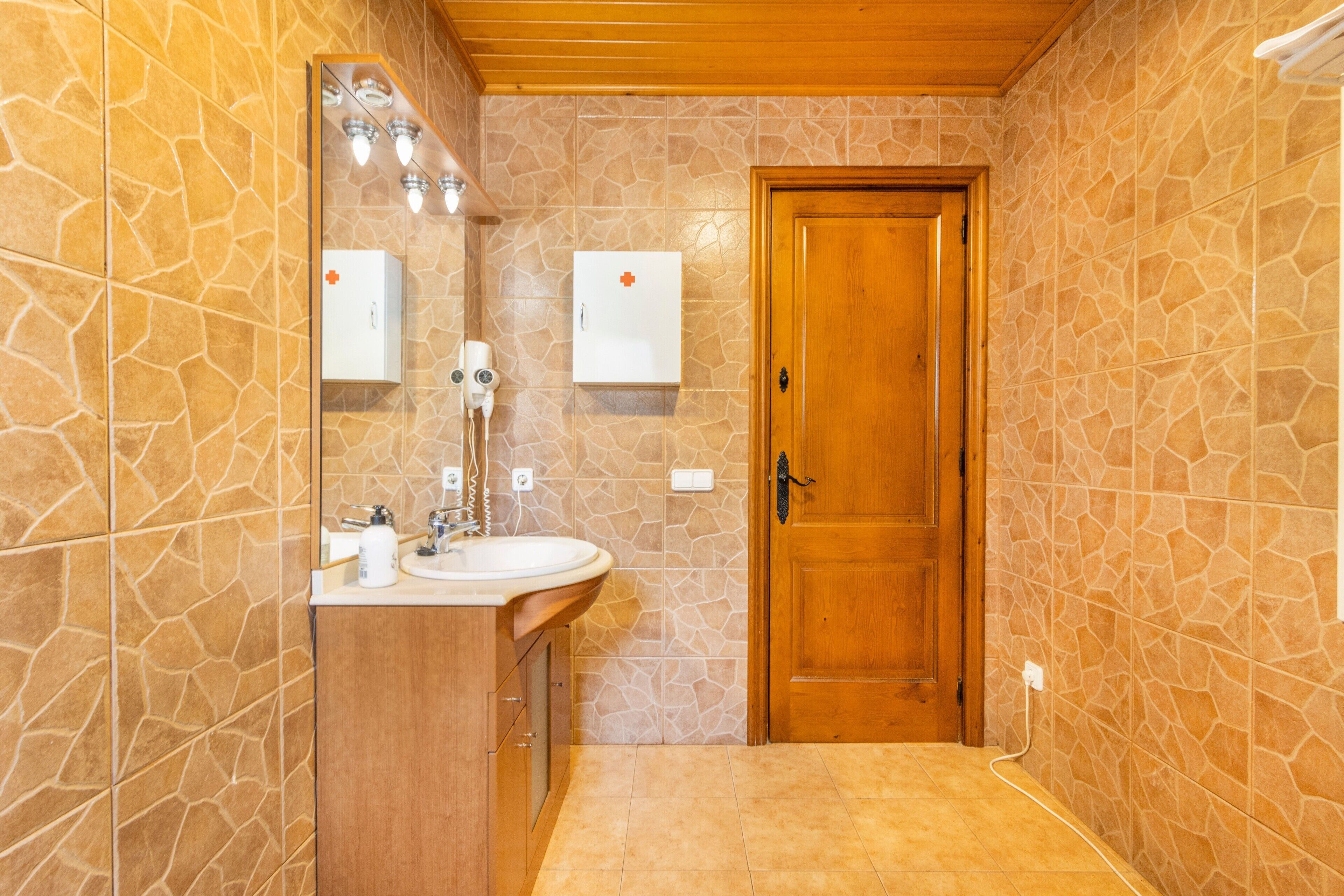 A bathroom with a wooden door, a sink, a mirror, and two white cabinets with red symbols.