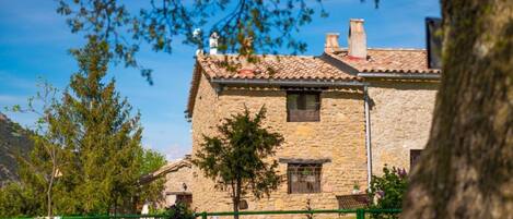 A stone building with a tiled roof, a small window, and a green fence in the foreground.