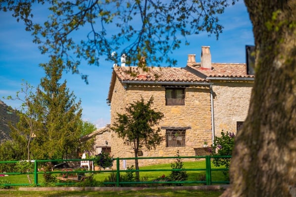 A stone building with a tiled roof, a small window, and a green fence in the foreground.