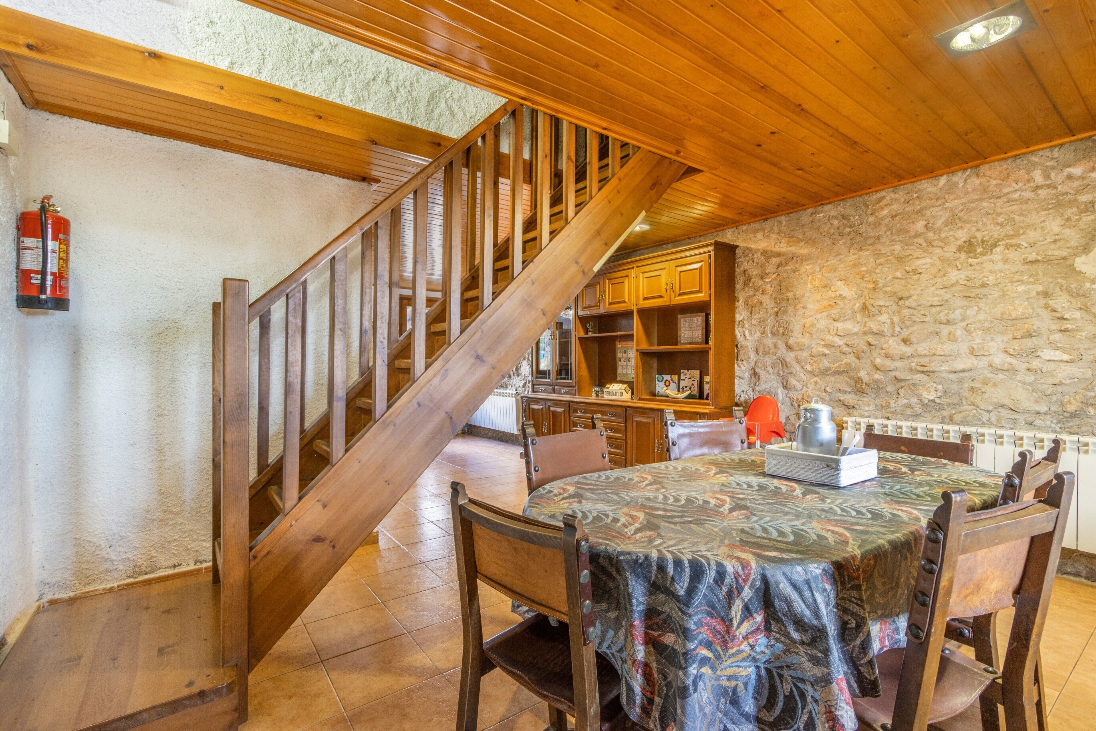 A wooden staircase leading to a dining area with a table set for two, a stone wall, and a kitchen area with cabinets.