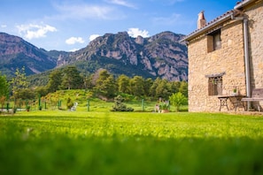 A stone building with a rustic appearance, a well-maintained lawn, and a mountainous backdrop.