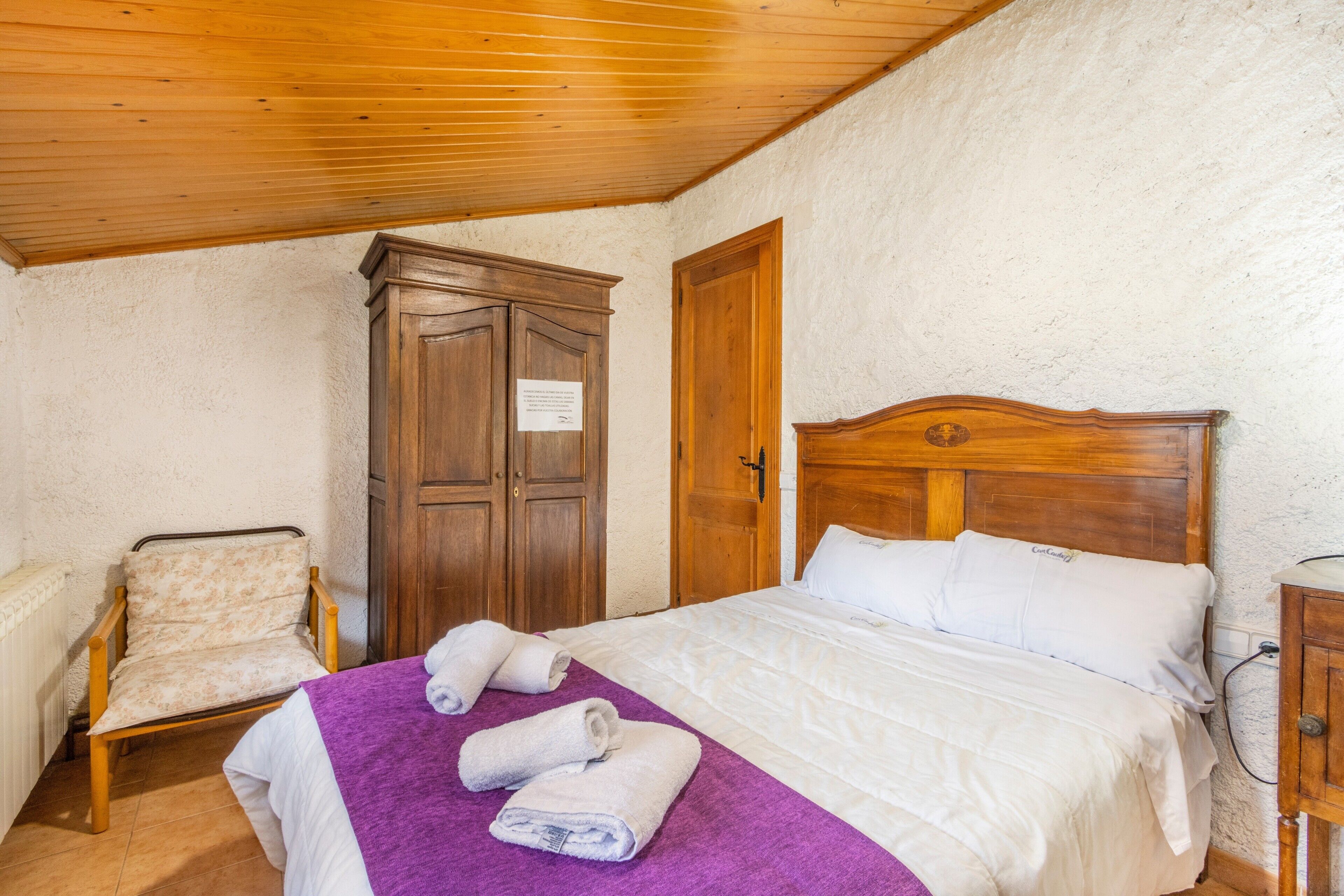 Une chambre à coucher avec un lit en bois, une chaise, une armoire et une petite table.