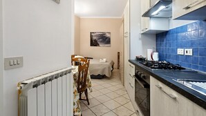 Una cocina compacta con estufa a gas, una mesa de comedor con sillas y un radiador.
