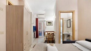 Habitación de hotel con cama, escritorio, silla, armario, baño con lavamanos y espejo.