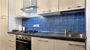 Una cocina moderna con armarios de madera clara, encimera negra, pileta de acero inoxidable y salpicadero de azulejos azules.