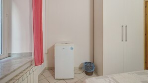 Una habitación con un armario blanco, un electrodoméstico pequeño de color blanco, una ventana con cortina roja y un radiador.