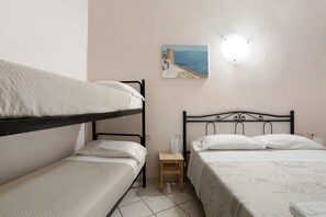 Une chambre avec des lits superposés, une petite table de chevet, une lampe fixée au mur et un tableau représentant un paysage côtier.