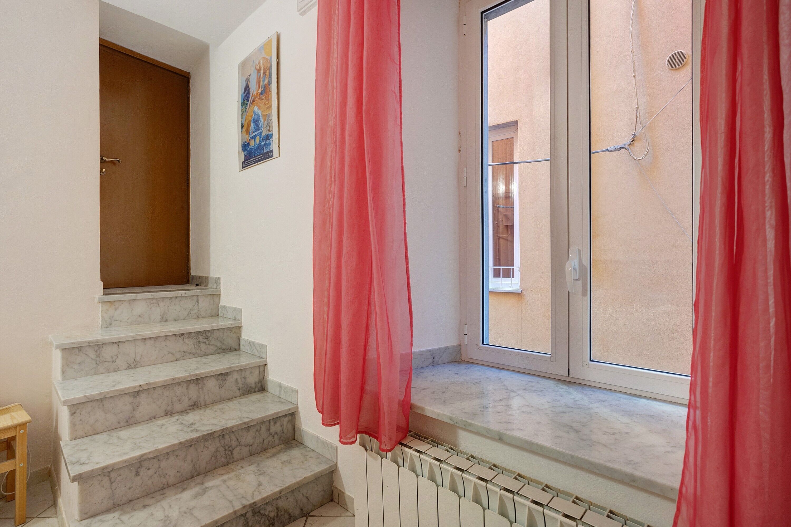 A staircase with marble steps leading to a landing, a window with a view of buildings, and a door.