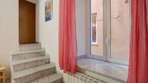 Una escalera con escalones de mármol que conduce a una plataforma, una ventana con vistas a edificios y una puerta.