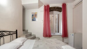 Un dormitorio con cama, radiador, refrigerador pequeño y ventana con cortinas rojas.